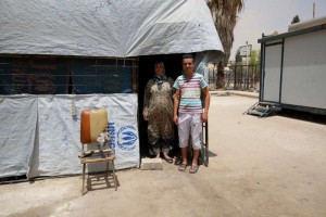أم عبد الوهاب مع ابنها البكر ماهر أمام الكشك الصغير الذي أسسته لكسب العيش داخل مركز إيواء خان دنون في مدينة الكسوة بريف دمشق/UNHCR