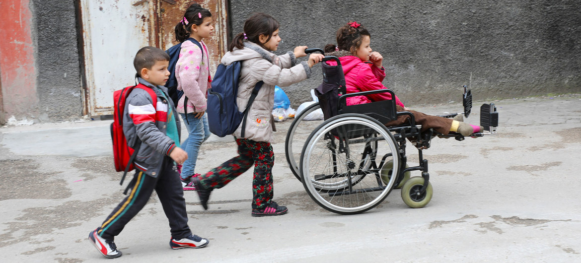 UNICEF/Can Remzi Ergen طفلة لاجئة من ذوي الإعاقة تجلس على كرسي متحرك تساعدها أختها بينما تتوجه هي وأشقاؤها إلى المدرسة في تركيا.